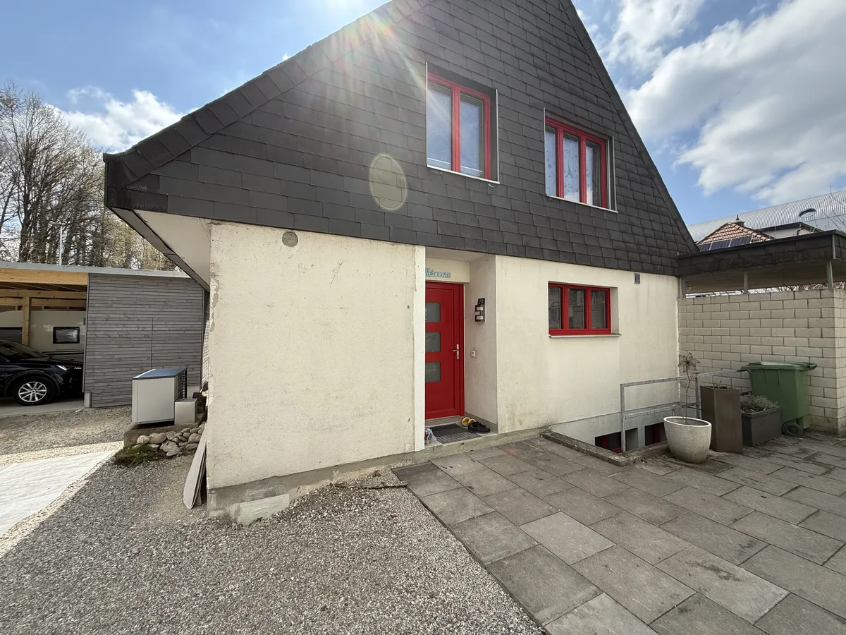 Einfamilienhaus mit roten Fenstern vor der Fassadenrenovation, Putz fleckig und rissig